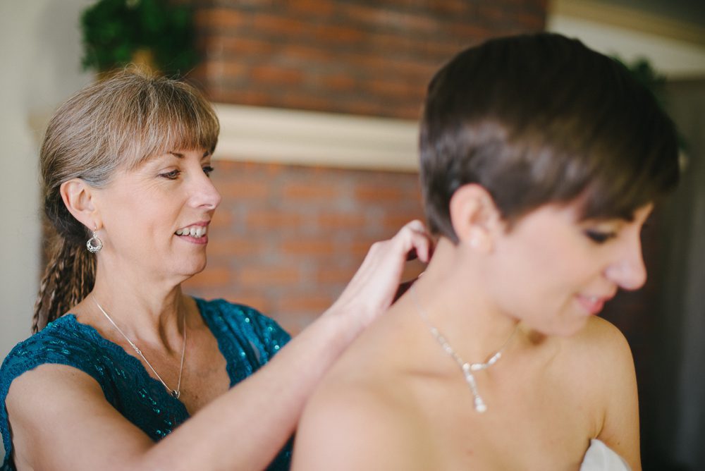 mother of the bride helping her put on her necklace
