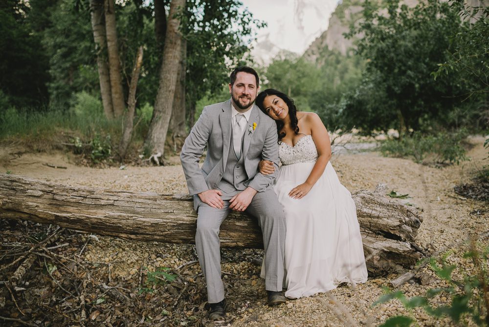 Bride and groom sitting on fallen tree with half dome in background