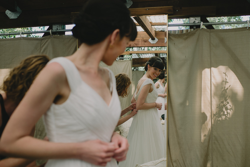 bride looking in mirror while putting on dress