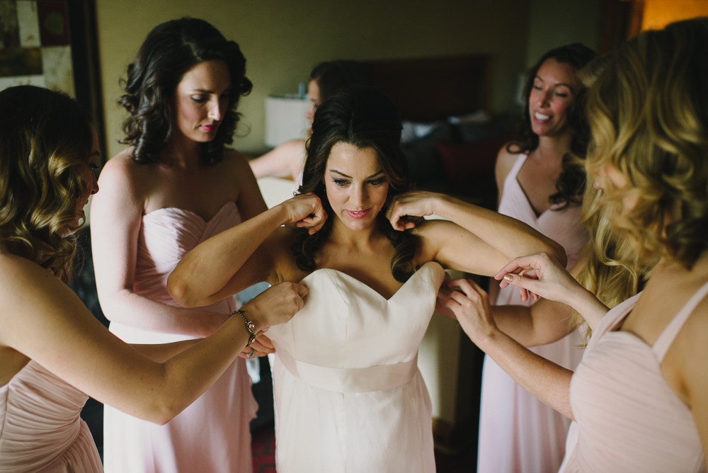 bride putting on her dress with bridesmaids