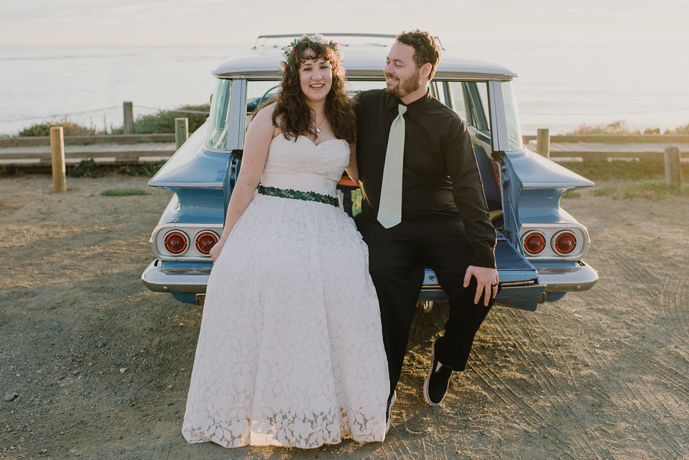 Bride and groom sitting in a classic blue car at sunset